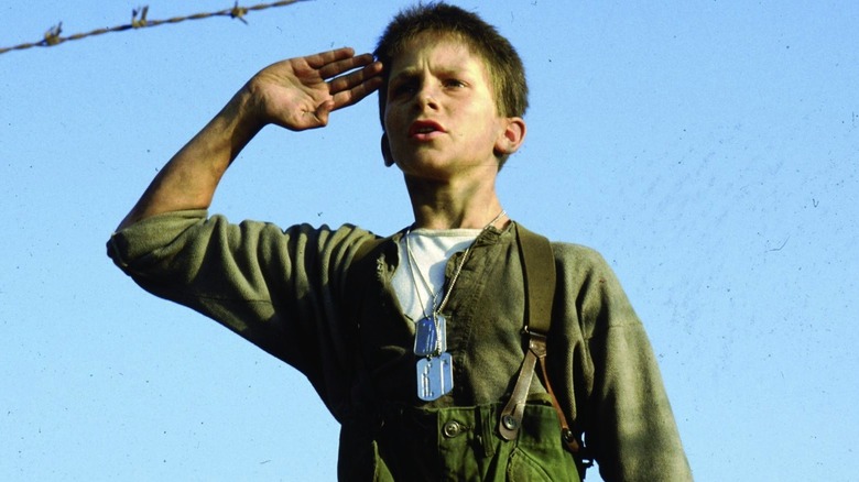 Jim salutes behind barbed wire in Empire of the Sun