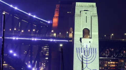 Getty Images It is dark and a pylon on the Sydney Harbour Bridge is illuminated in white light and features a menorah.