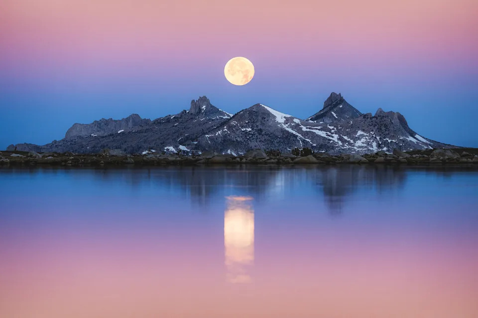 a moon rises over mountains in front of a lake in Yosemite National Park, California