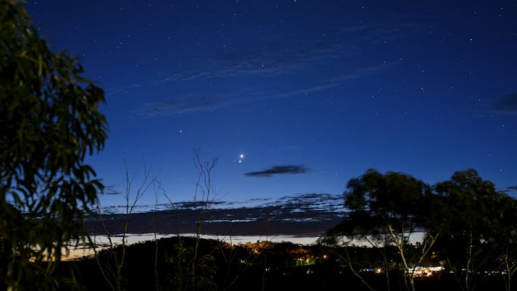 A dark nightscape with two bright stars very close together above the horizon.