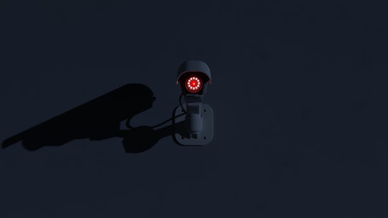 Surveillance camera with red lens glowing in the dark.