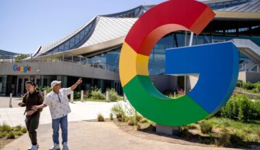 Two people walk past a large Google logo sculpture in front of the Bay View campus building in Mountain View, California.