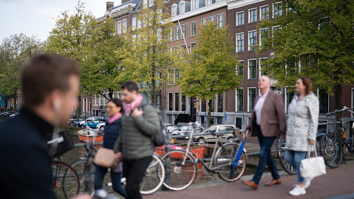 People walk across a bridge over the Keizersgracht canal in Amsterdam with bicycles parked nearby.