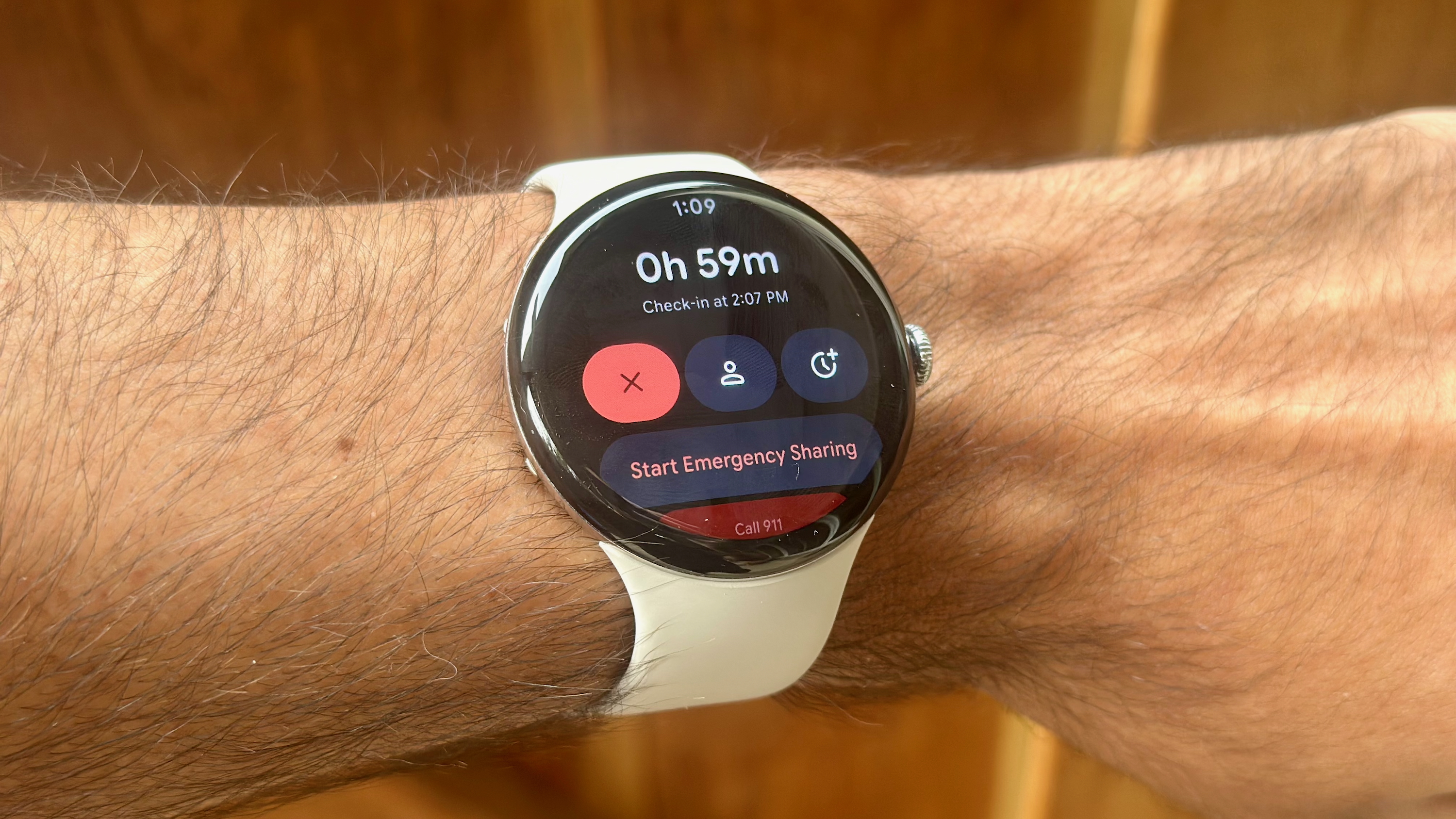 A photo of the Google Pixel Watch 4 showing a Safety Check activity, with an hour left and options to Start Emergency Sharing or Call 911.