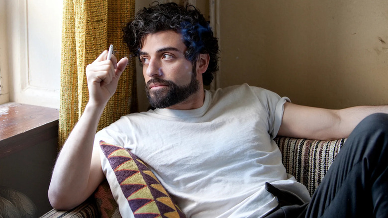 Oscar Isaac as Llewyn Davis, leaning back in a chair with a cigarette in Inside Llewyn Davis
