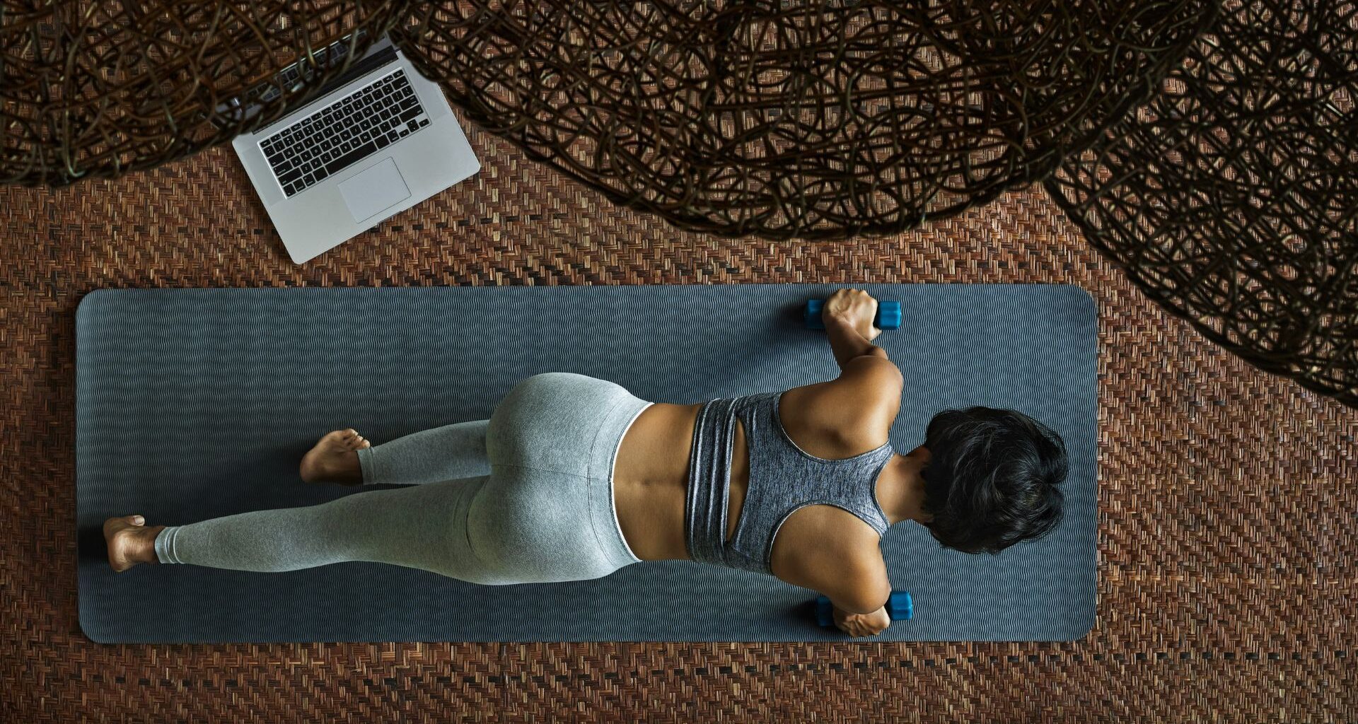 Woman doing 20-minute workout on yoga mat in living room next to open laptop