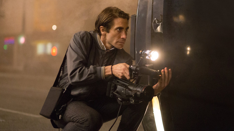 Jake Gyllenhaal as Louis Bloom, kneeling with a camera in Nightcrawler