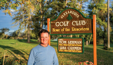 Man standing next to a sign reading Alexandria Golf Club, Home of the Resorters