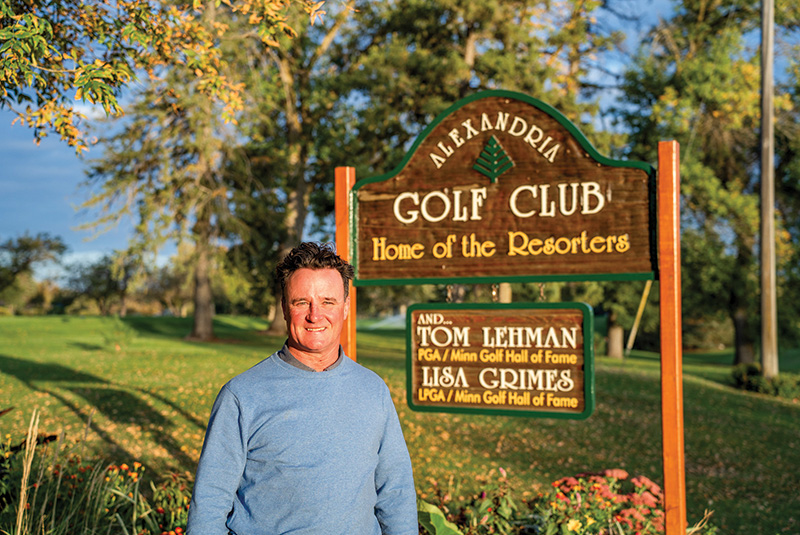 Man standing next to a sign reading Alexandria Golf Club, Home of the Resorters