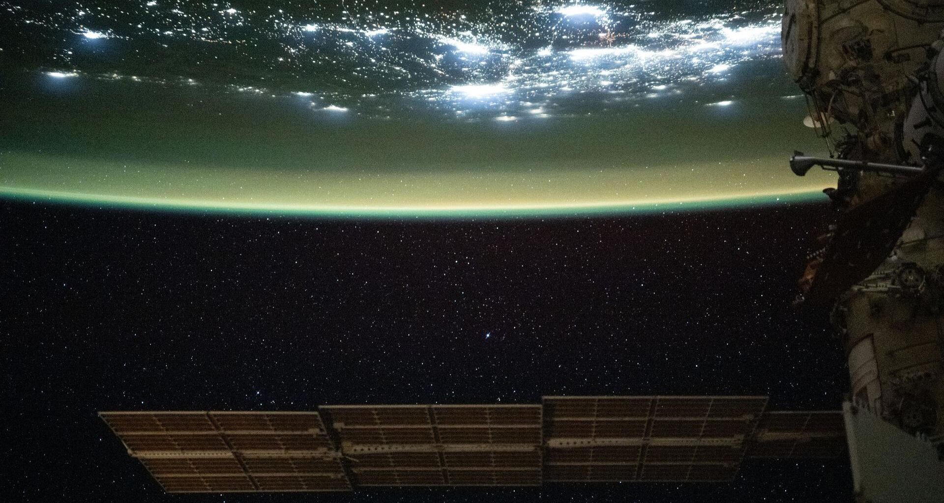 A large solar array is seen at the bottom of this image floating in space as the top half of the image shows Earth with a green sheen over its surface
