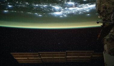 A large solar array is seen at the bottom of this image floating in space as the top half of the image shows Earth with a green sheen over its surface