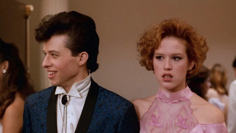 Jon Cryer as Duckie in blue suit and bolo tie next to Molly Ringwald as Andie in pink dress in Pretty in Pink