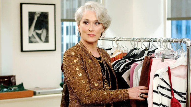 Meryl Streep as Miranda Priestley in gold top standing next to clothing rack in The Devil Wears Prada