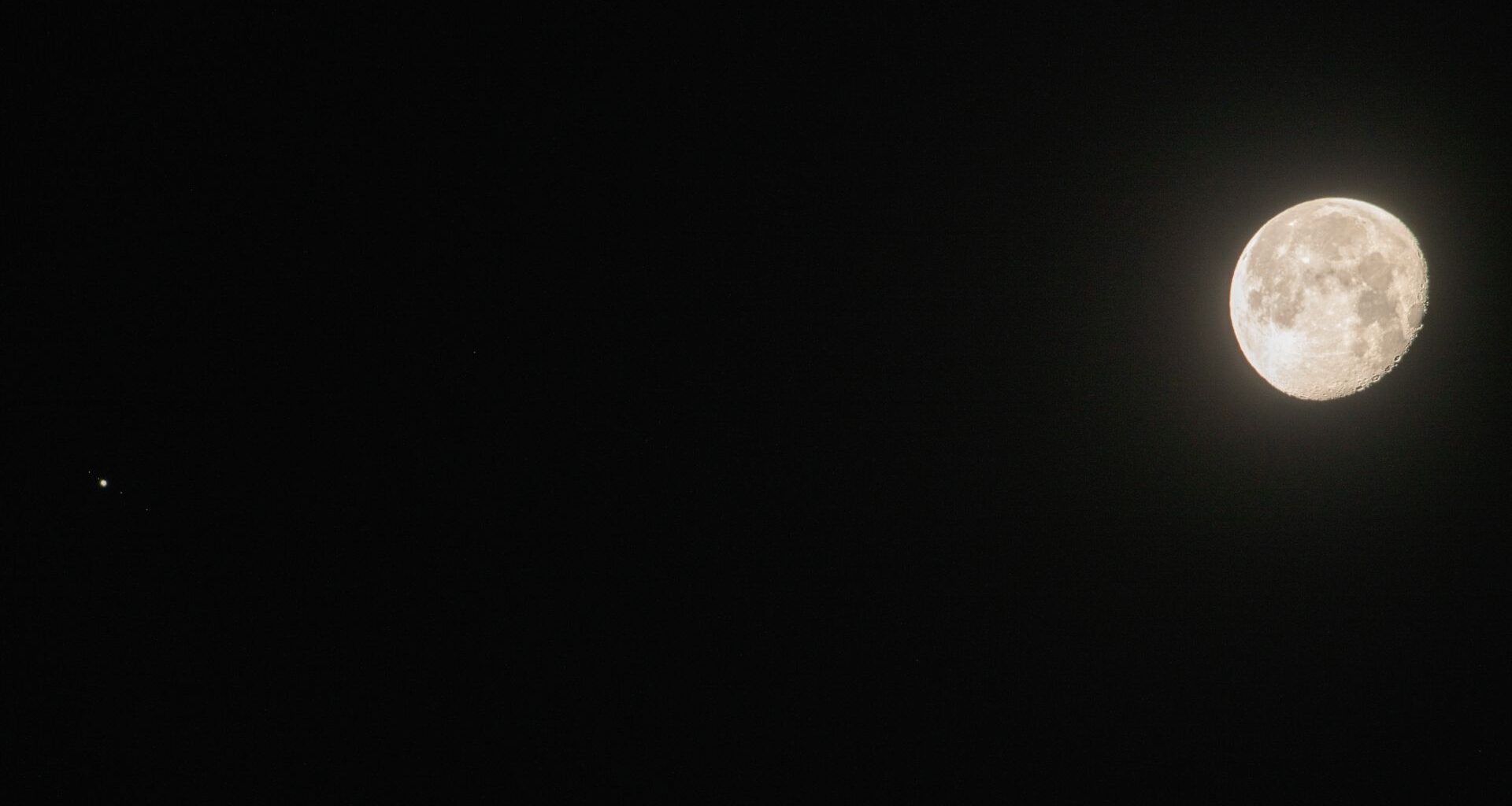 A near-full moon shines to the right of an image of the black night sky, while a small point of light representing Jupiter can be seen to the left of the image.