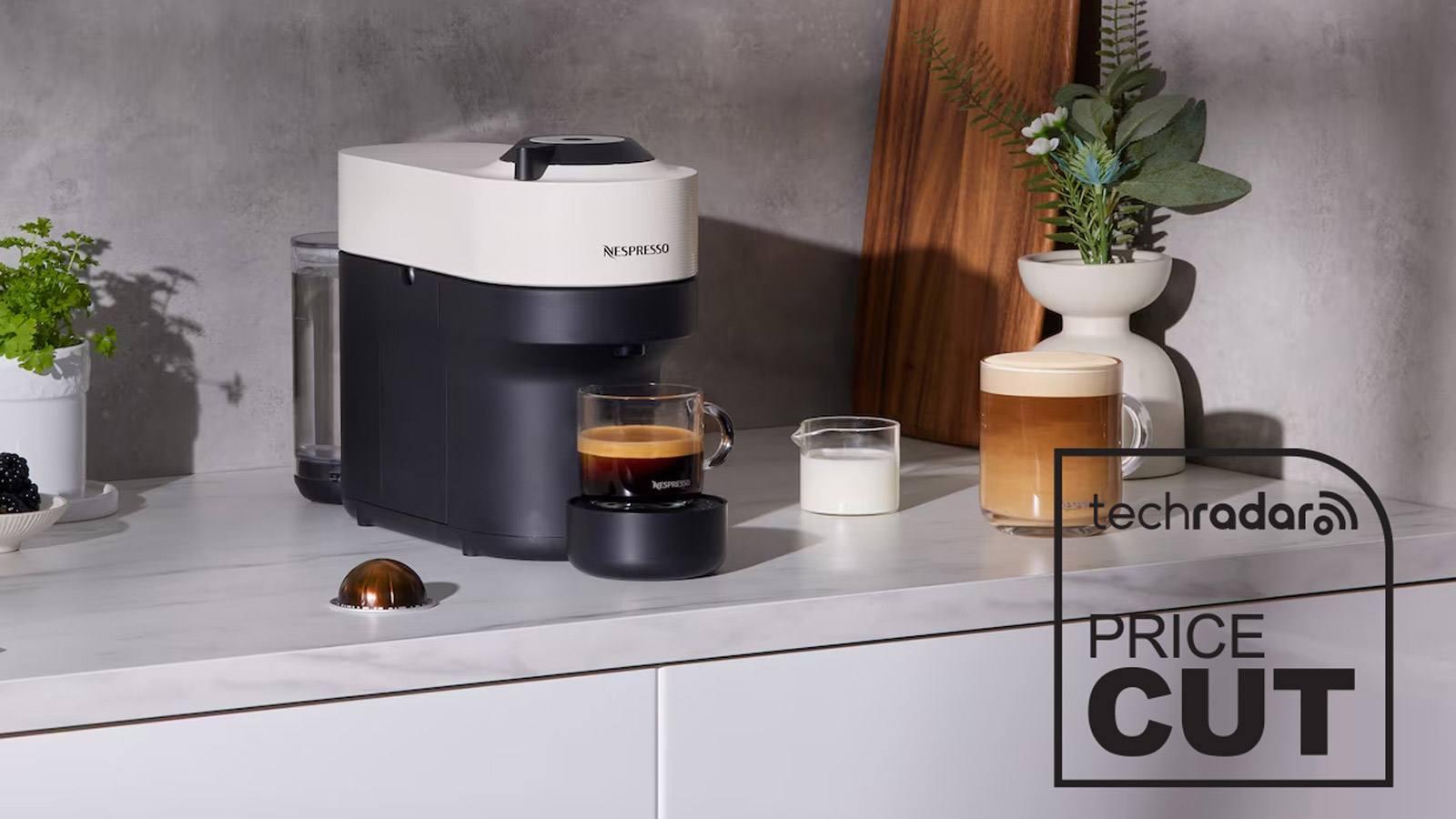 Nespresso Vertuo Pop in Coconut White, on a kitchen counter. A poured espresso shot in a glass cup is under the machine's spout, and another full coffee with milk is to the right.