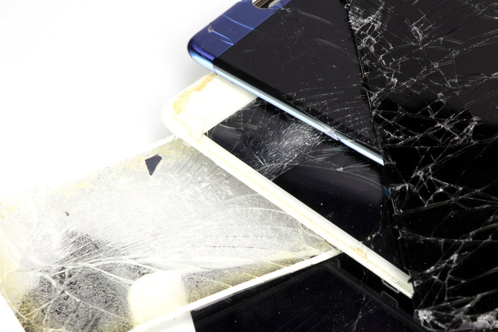 Several stacked smartphones with smashed screens.