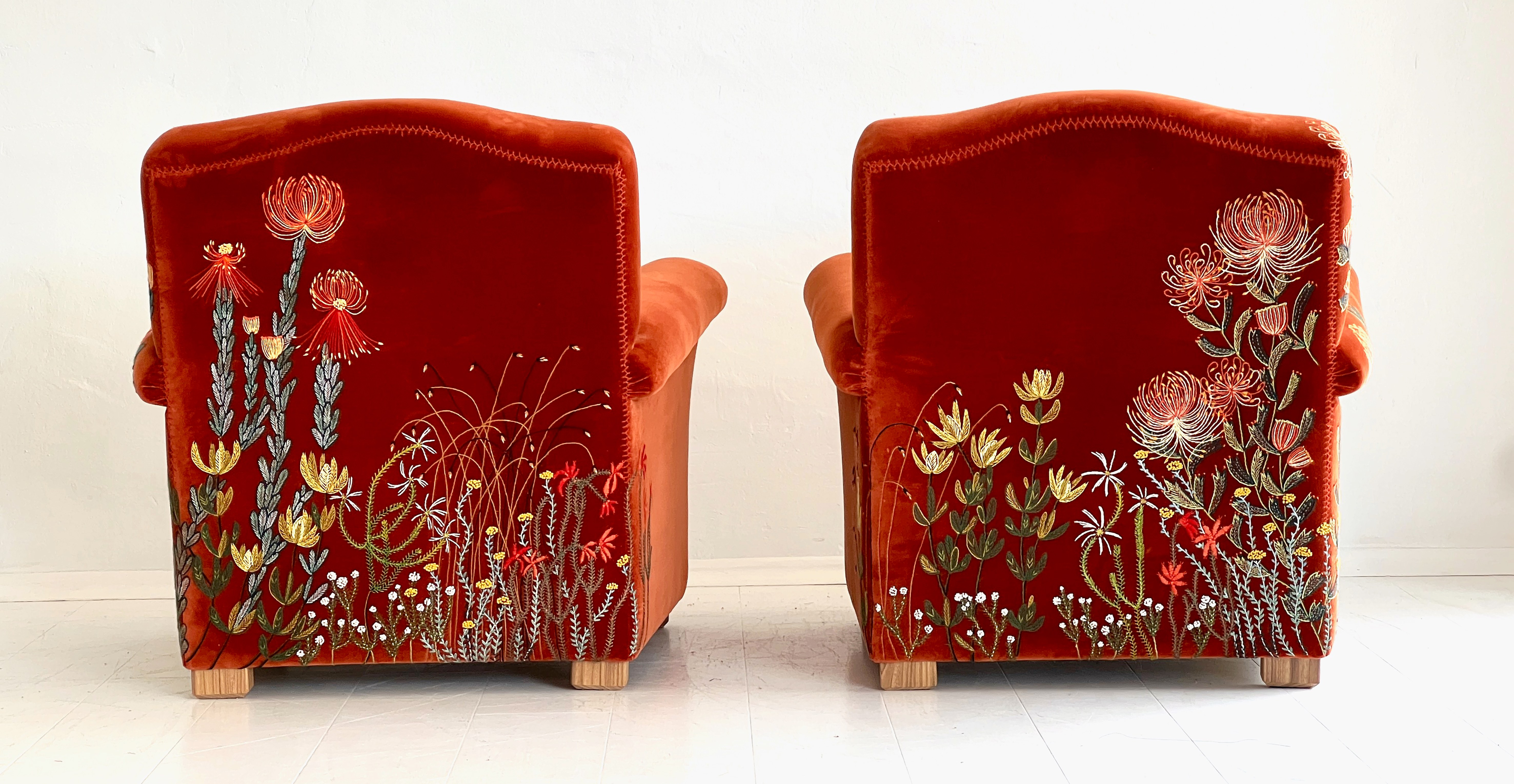 Two orange velvet armchairs with embroidered flowers on their backs.