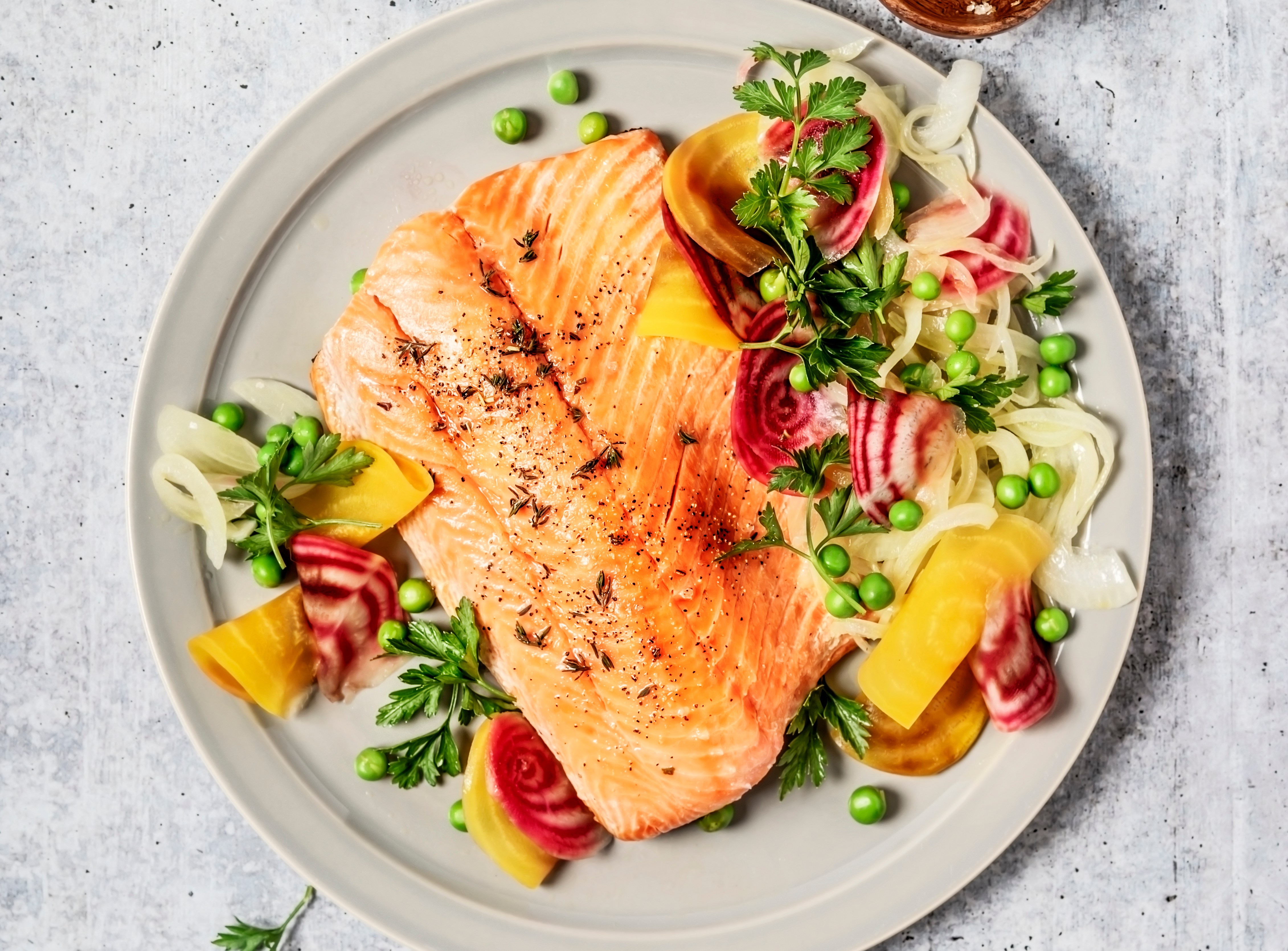 Pan-fried salmon with vegetables on a gray background.