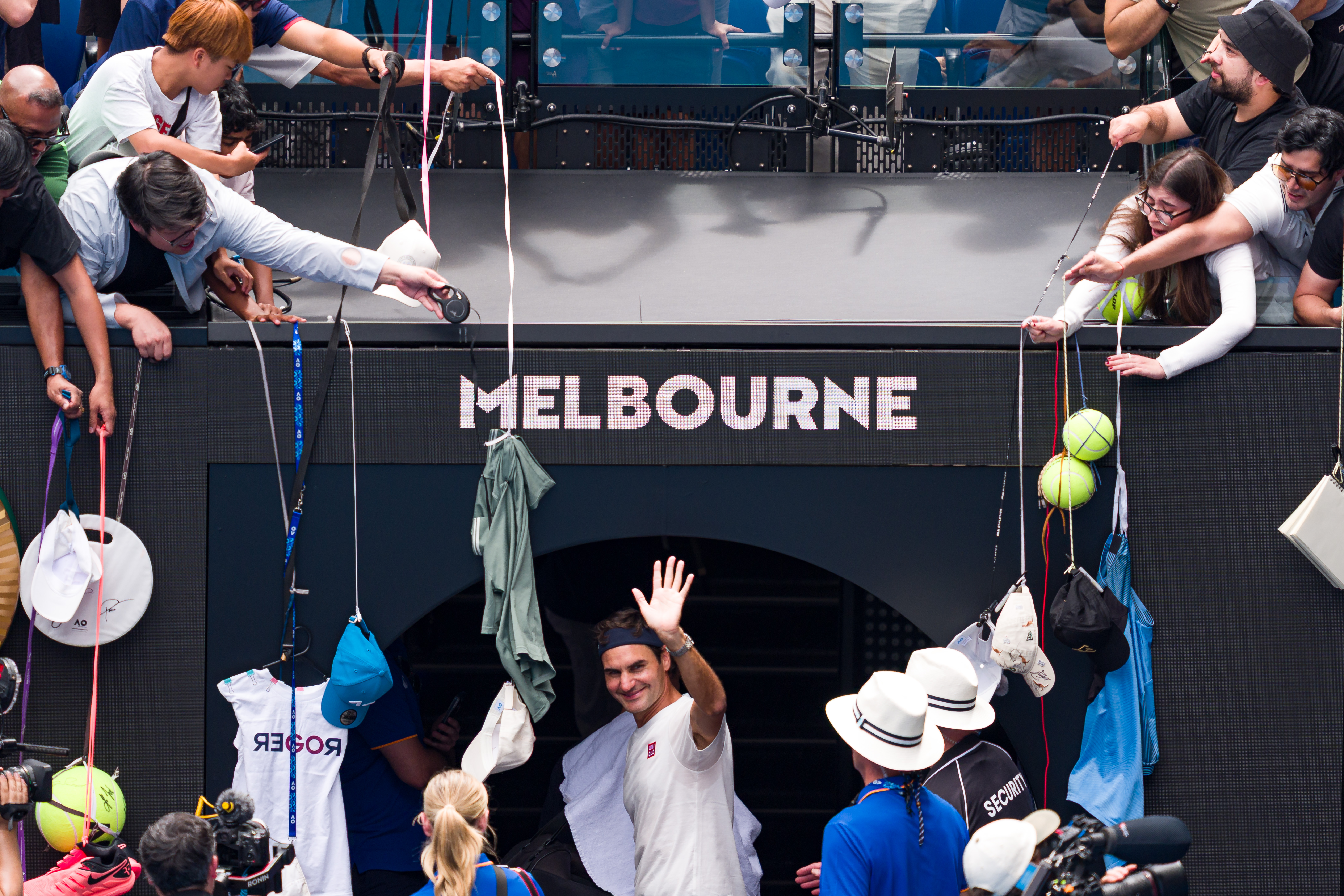 Roger Federer waves to fans from beneath a "MELBOURNE" sign as fans reach out with memorabilia to be signed.