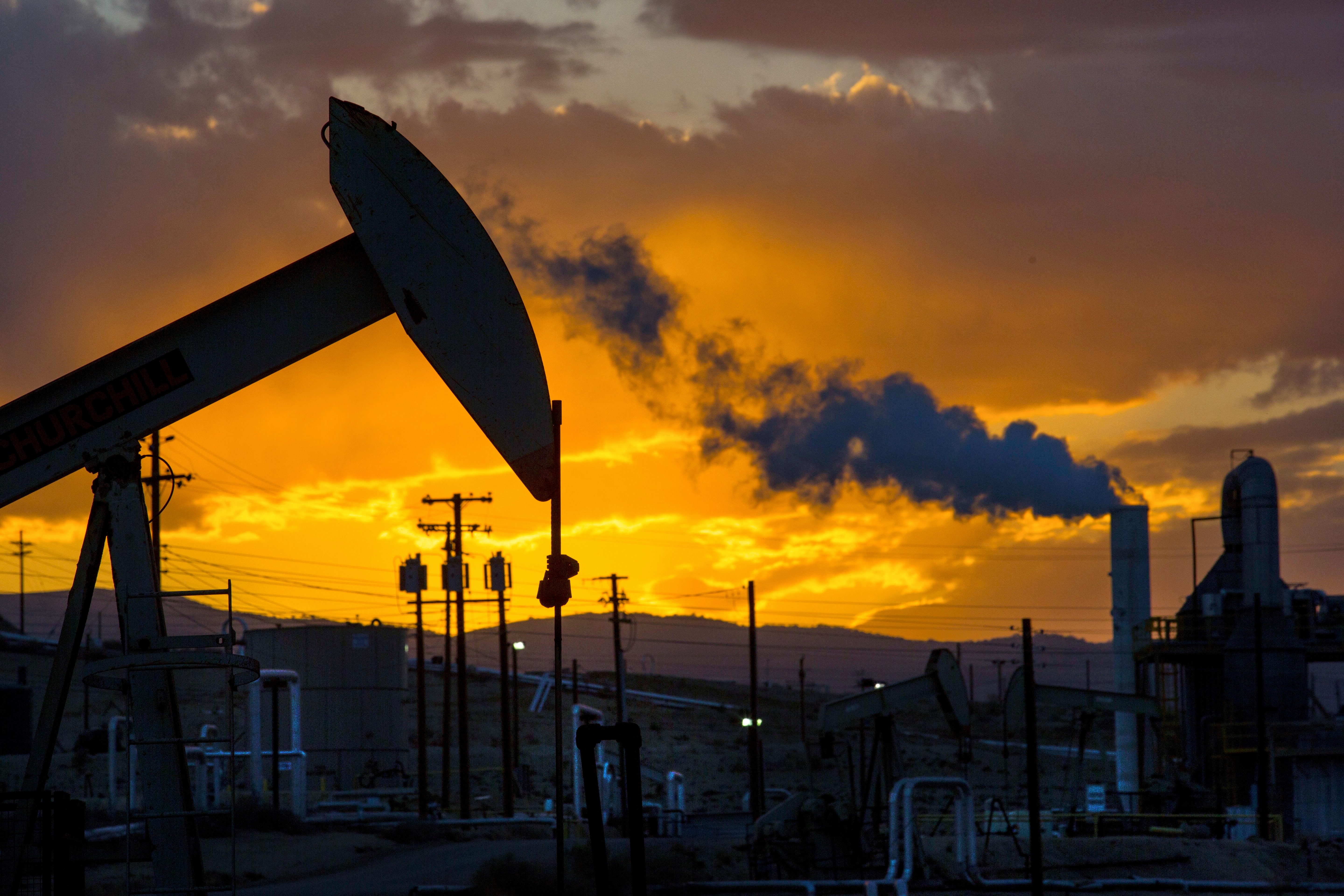 Oil field at sunset in California with pumpjacks and smoke plumes.
