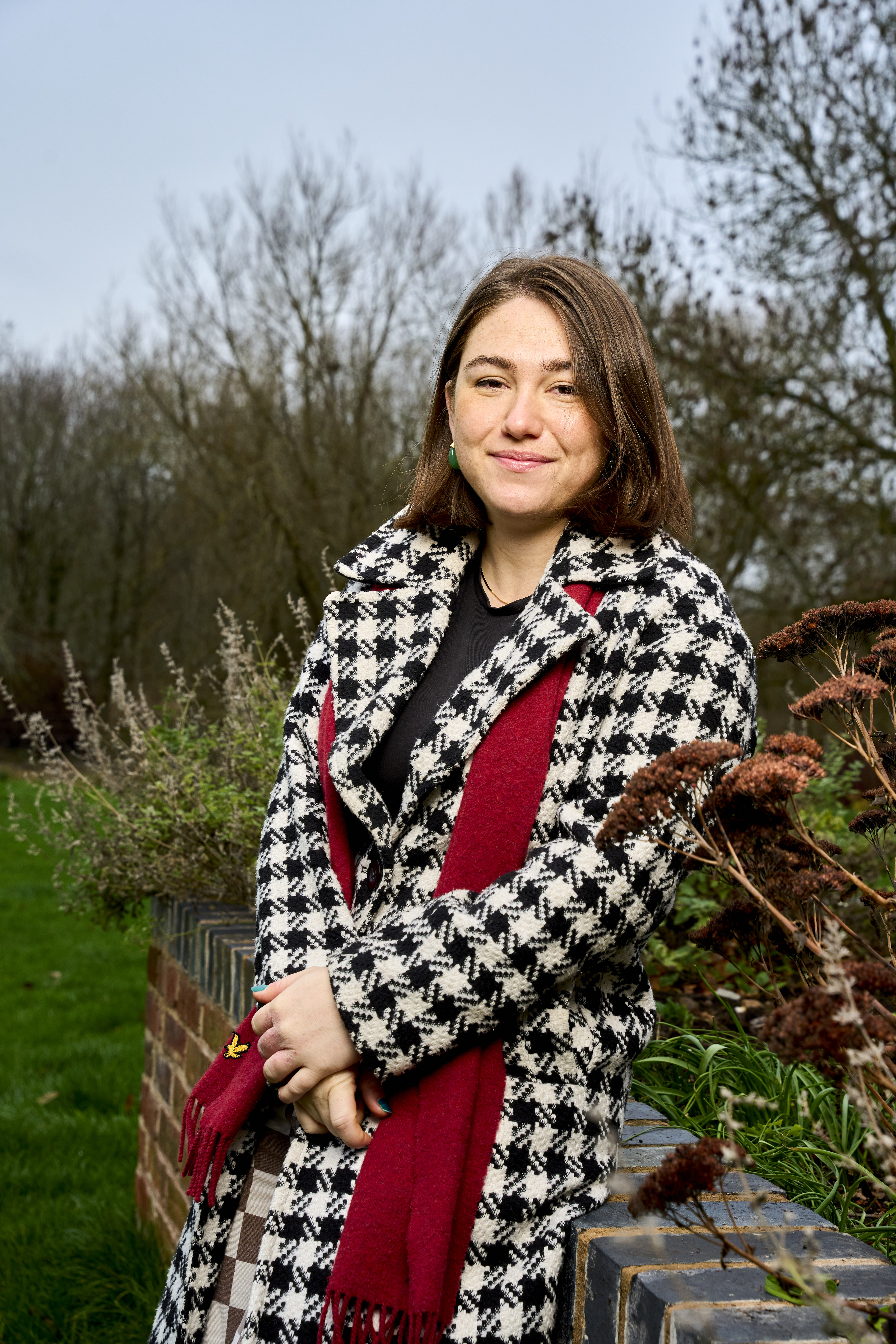 Sophie Samuda, TV producer and former Kissing it Better volunteer, stands outdoors in a black and white houndstooth coat and red scarf.