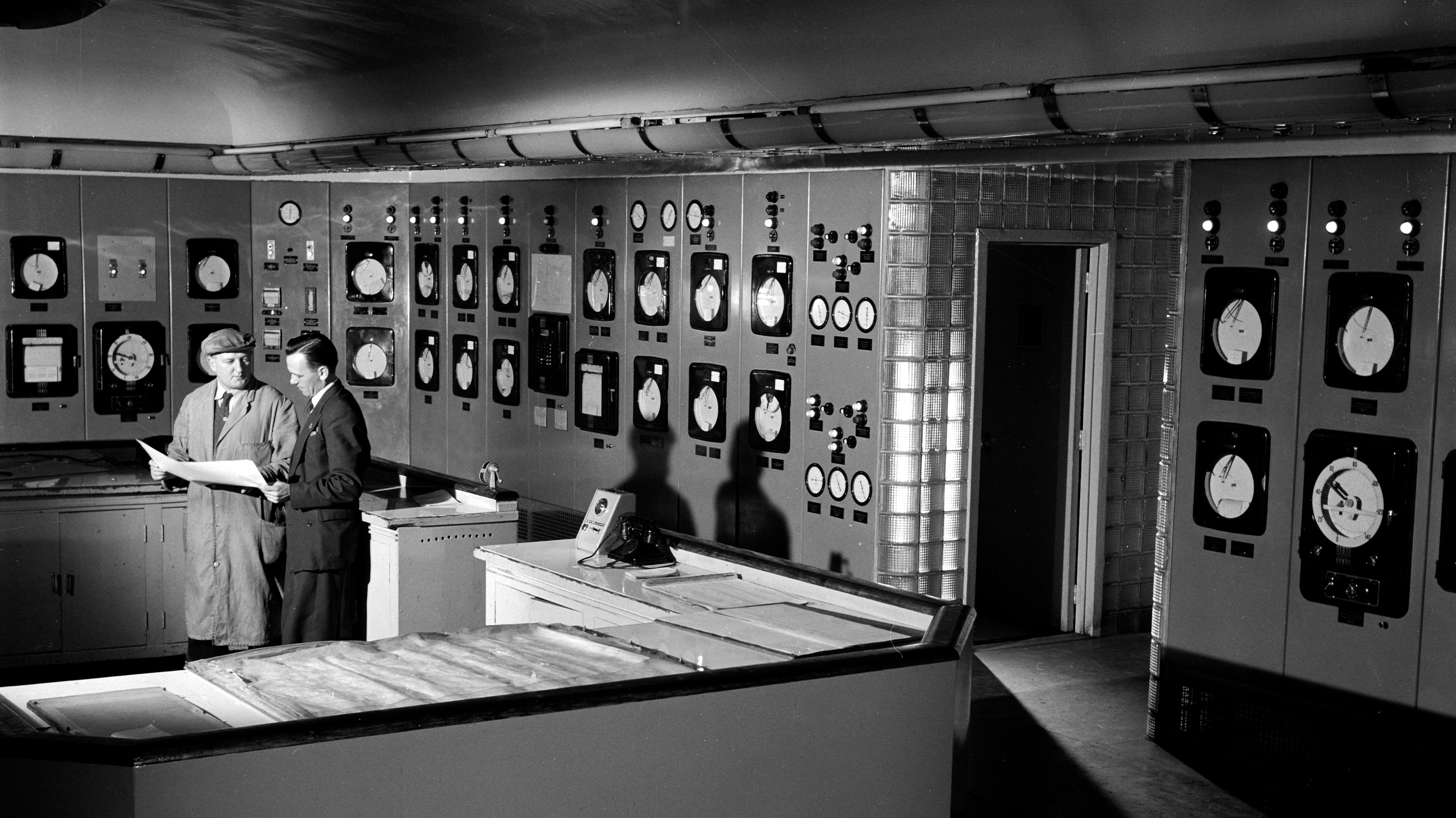 Two men in a control room for a plastics plant, looking at blueprints.