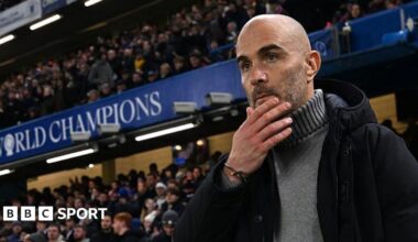 Enzo Maresca, manager of Chelsea, looks on prior to the Premier League match between Chelsea and Bournemouth at Stamford Bridge. He is wearing a grey jumper beneath a dark coat.