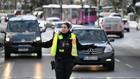 AFP via Getty Images A policewoman wearing a high visibility waistcoat directs traffic on a road in Berlin where traffic lights have been out of action due to the power outage. 