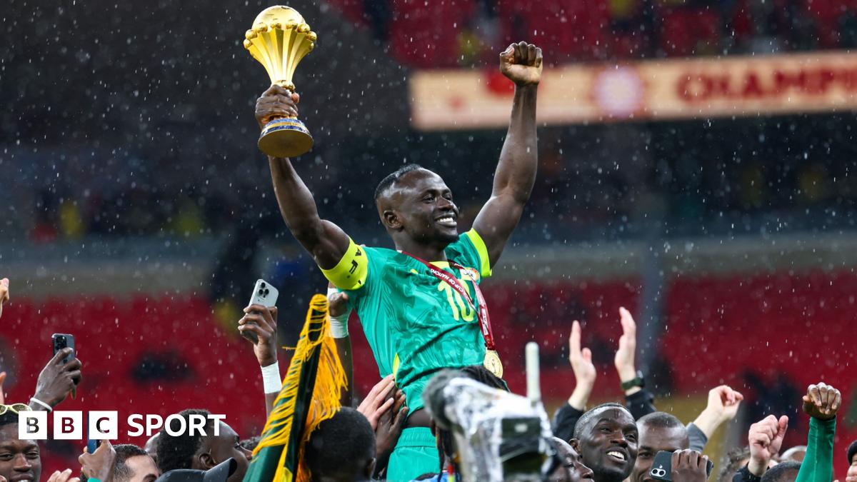 Brahim Diaz in all-white Morocco kit is seen on the left side of an image, chipping a penalty straight into the arms of Senegal goalkeeper Eduoard Mendy, all in blue on the right of the image, in the final of Afcon 2025. Mendy waits, bent slightly over, to collect the ball which is nearing him