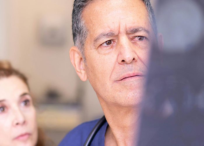 Middle-aged doctor reviewing X-ray with concerned expression while patient looks on during medical consultation