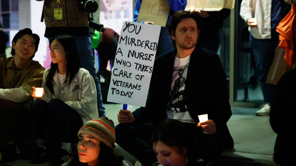 A demonstrator seated on a street curb holds and candle in one hand and a sign in the other that reads, "You murdered a nurse who takes care of veterans today."