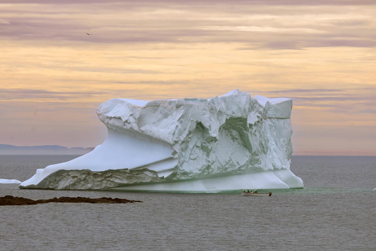 an iceberg on water with a boat with people alongside it. 