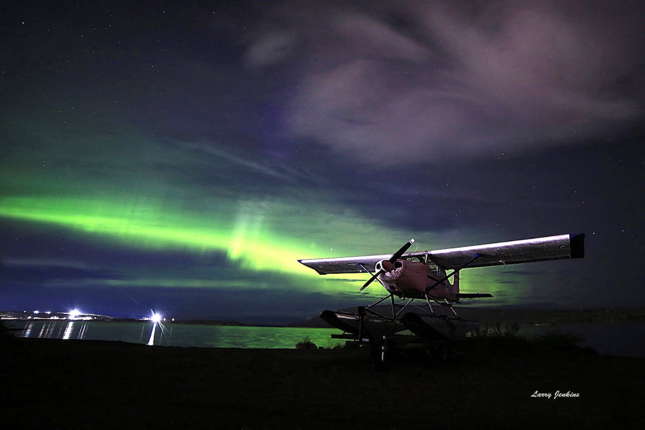 Plane in front of the water at night. Green northern lights in the sky.