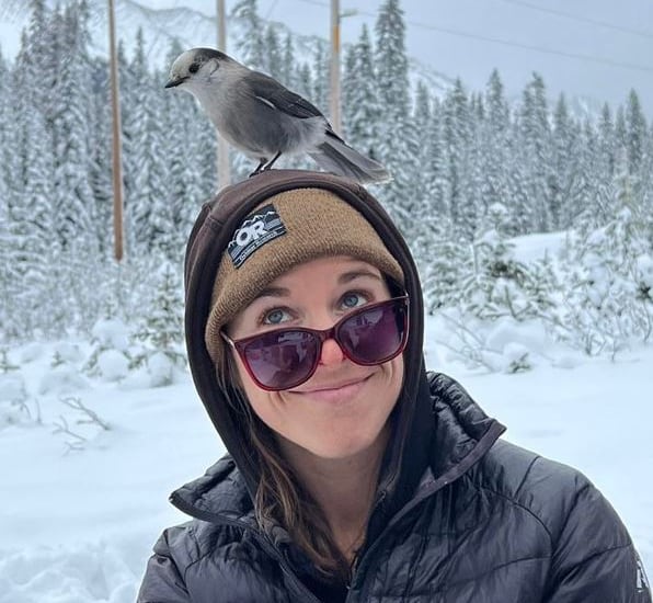 A woman smiles with a bird on her head.