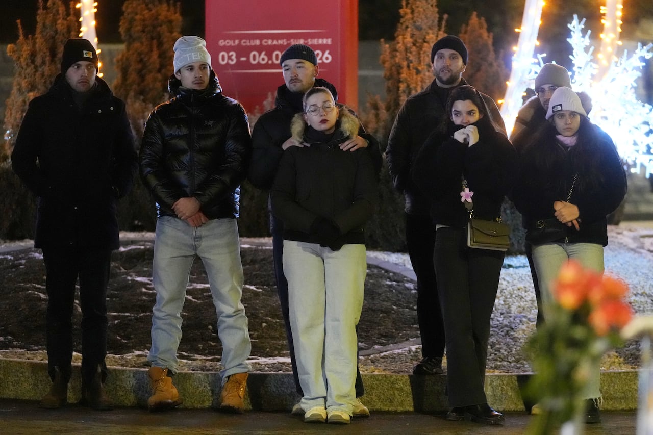 A group of young people, dressed in winter clothig, stand in a row with downcast expressions.