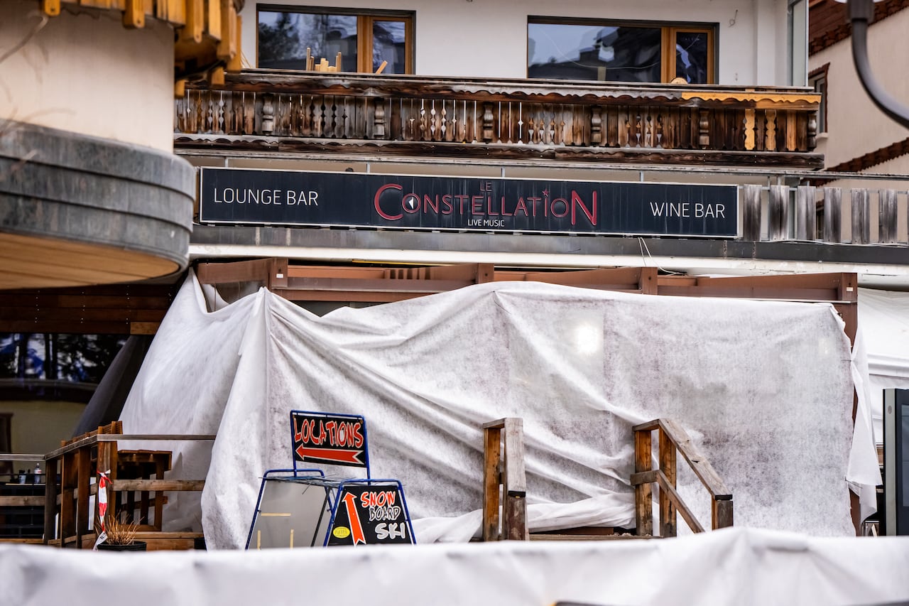 A white tarp hangs in front of the entrance to a bar with a black sign, with read letters that read "Le Constellation," above.