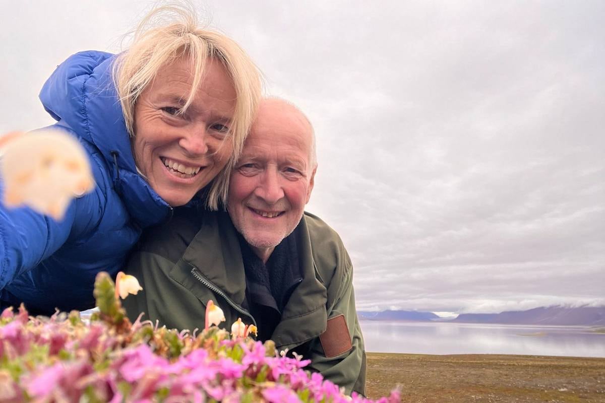 woman and man stand on land with ocean in background and flowers in forefront