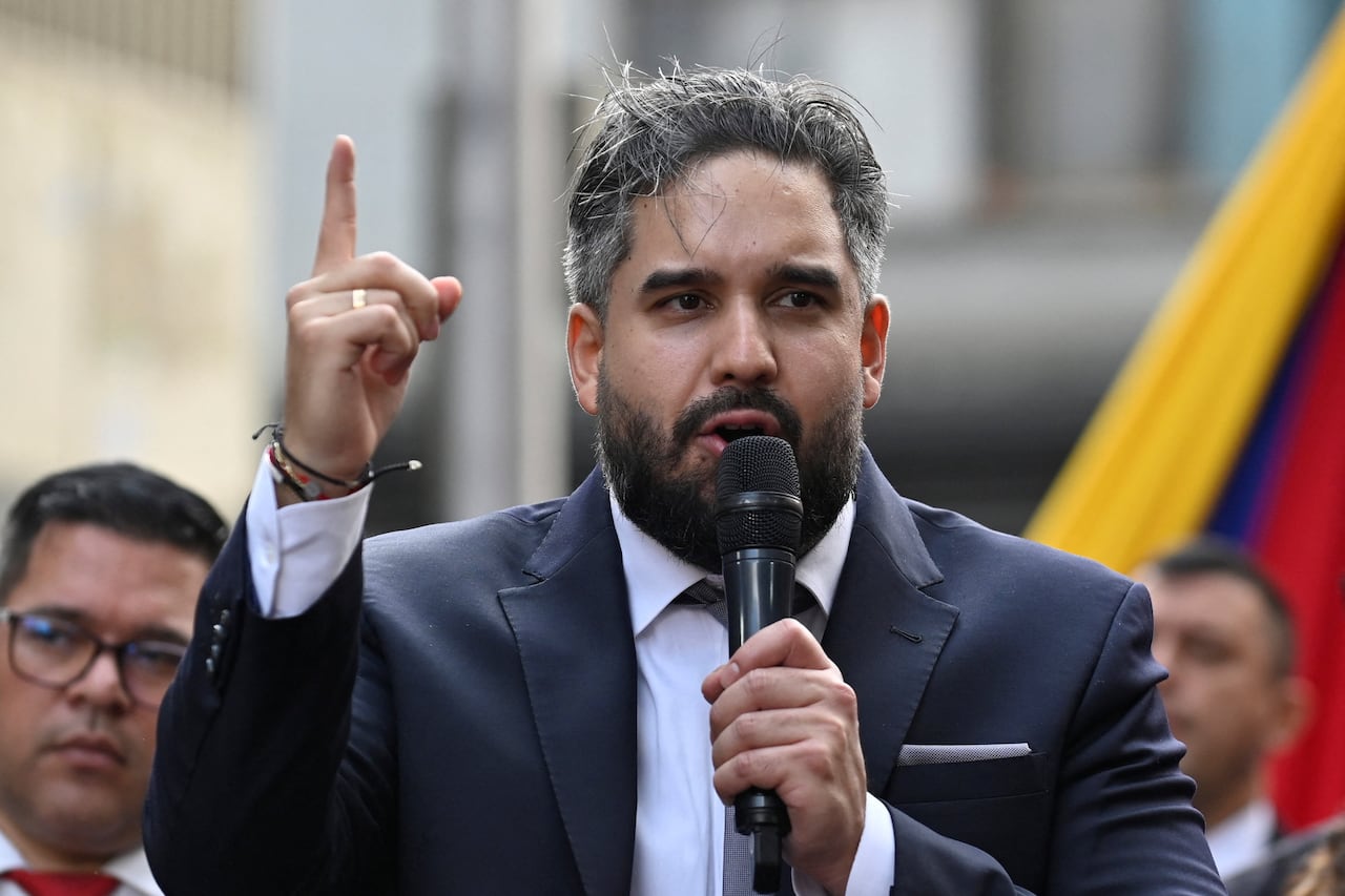 Man in suit speaking into a microphone while pointing a finger at sky