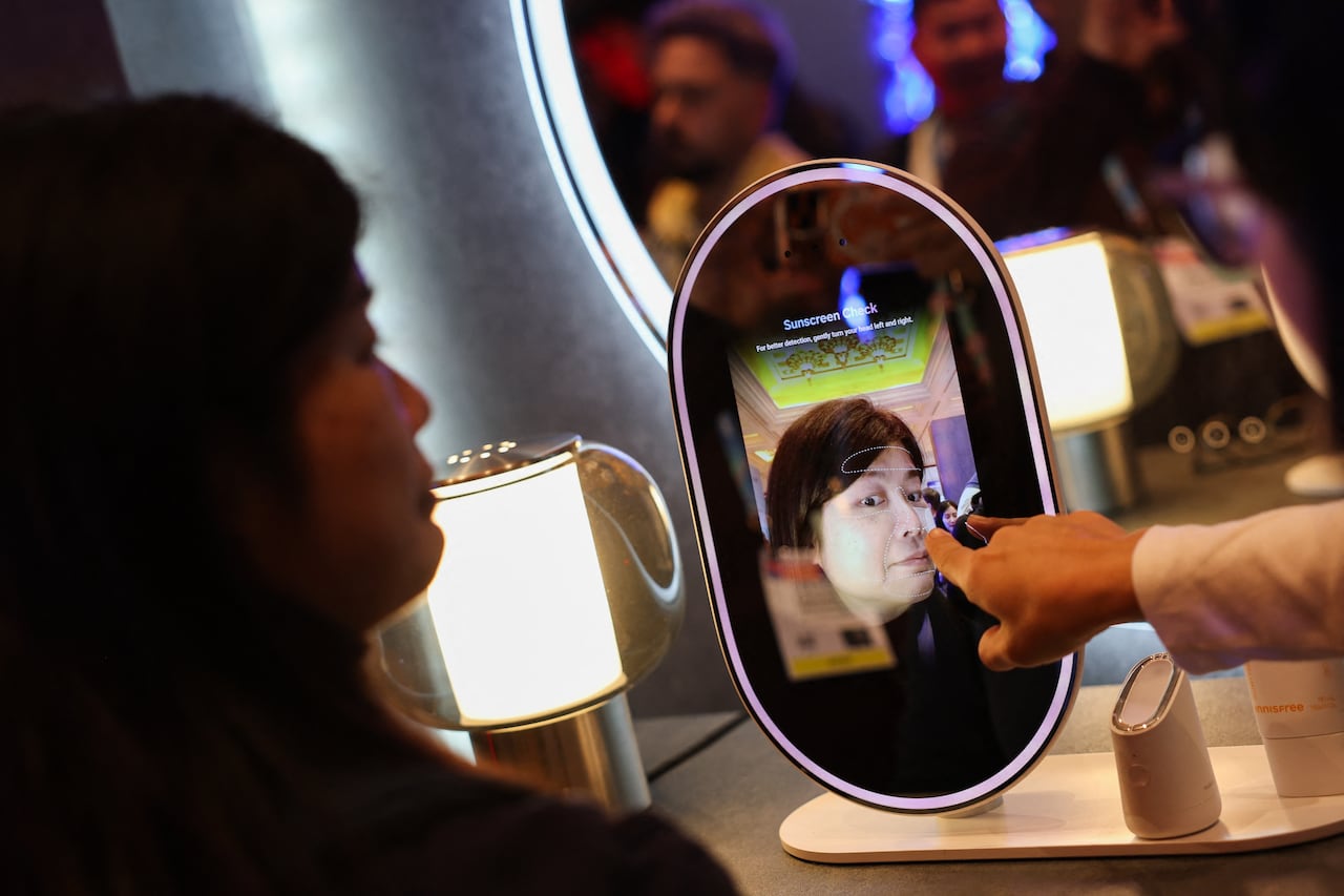 A person facing an oval screen that resembles a mirror, with another person's hand pointing at her reflection on the device.