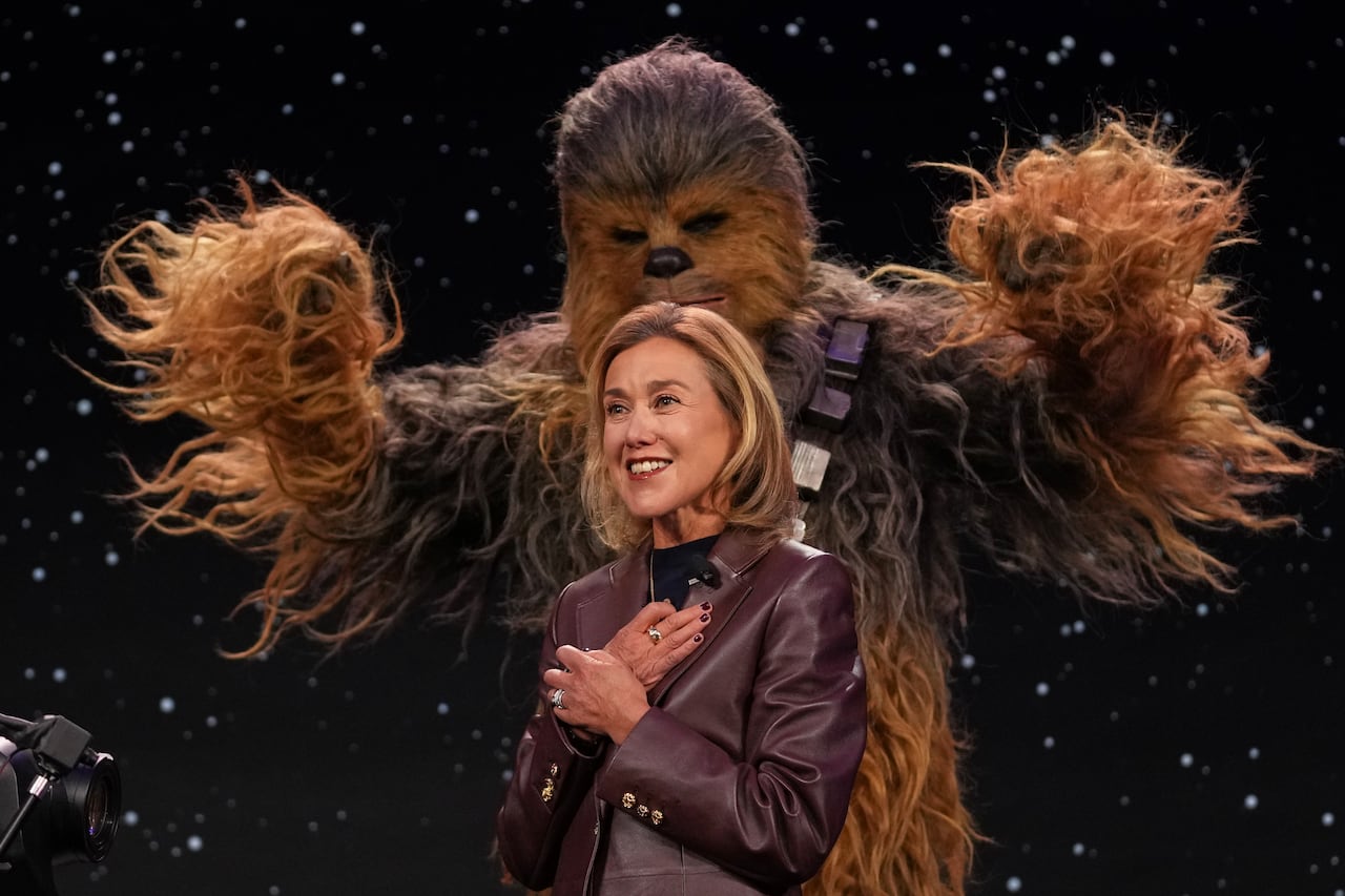 A person in a Chewbacca from Star Wars costume stands behind a woman on stage.