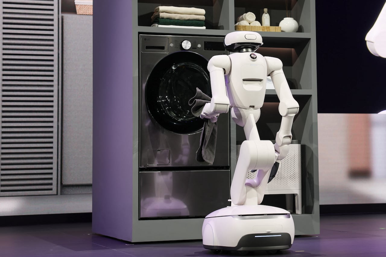 During a demo on stage, a white robot loads a towel into a front-loading washing machine