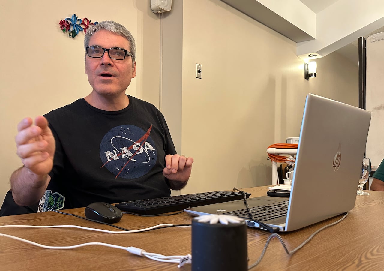 A man sits at a table with a laptop and a speaker.