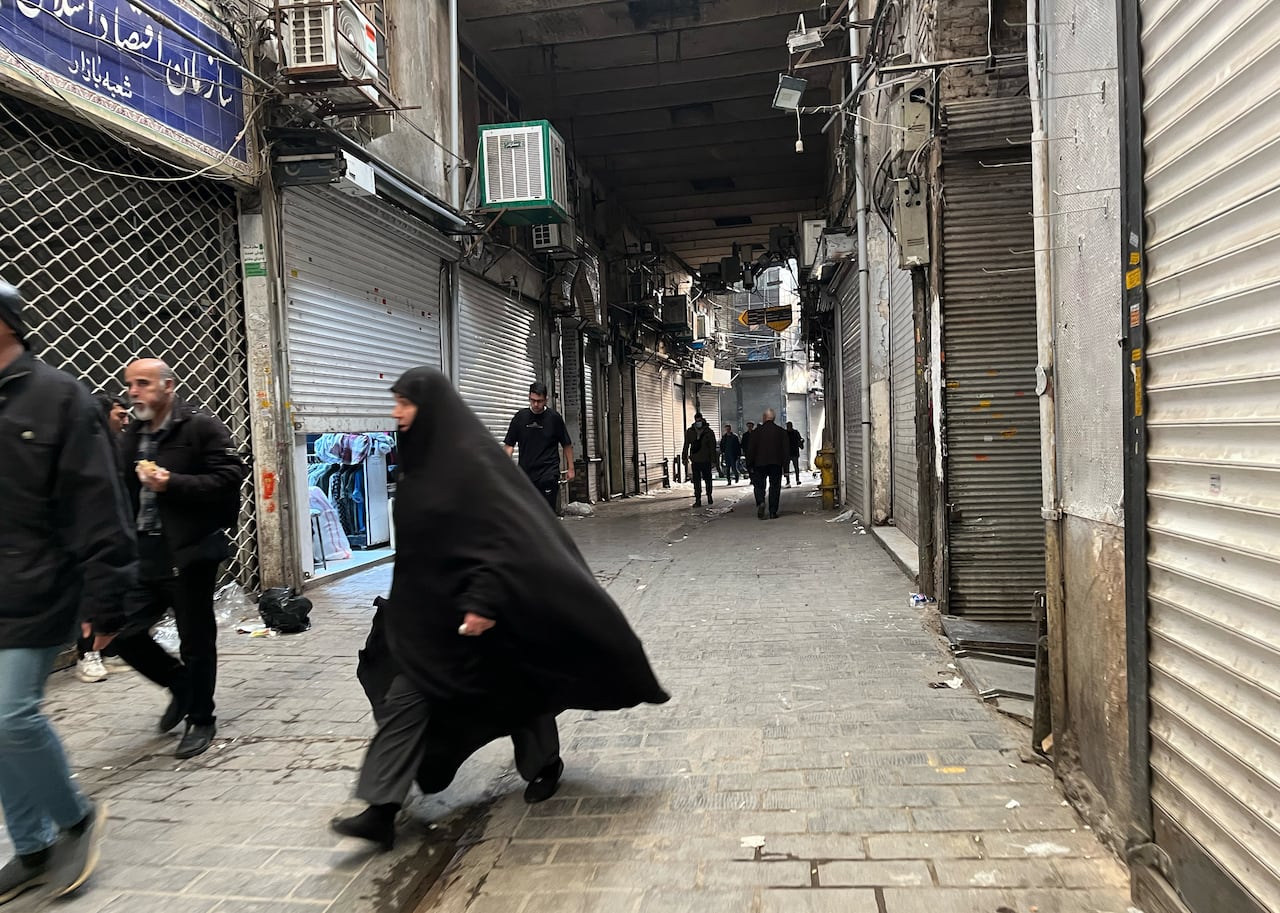 People walk down a street with stores shuttered on either side.