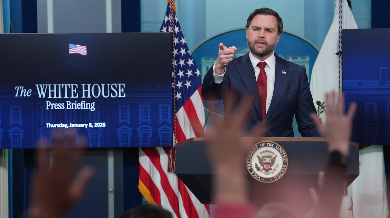  JD Vance points toward reporters as some raise their hands. A monitor shows the words "White House Press Briefing, Thursday, January 8, 2026.'