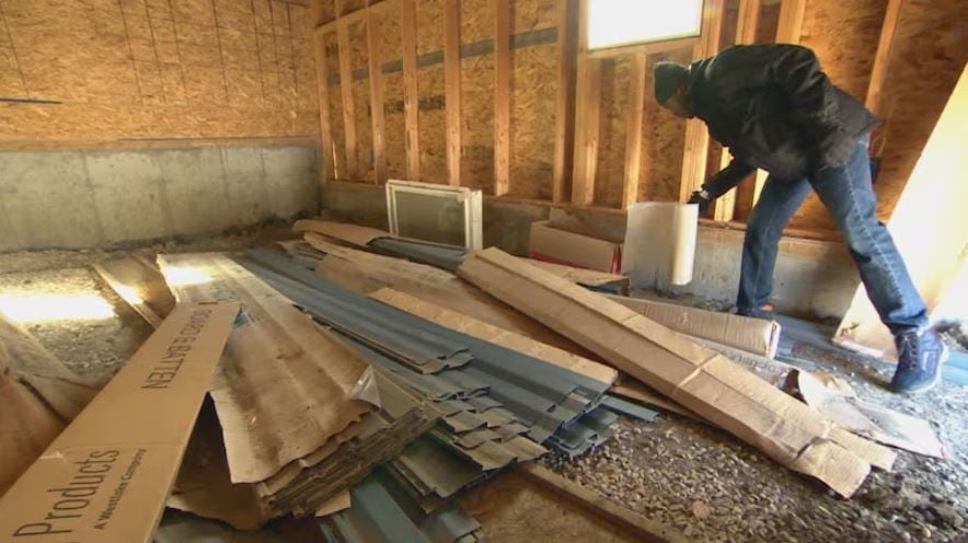 A man leans across timber and other materiel in a partly constructed room