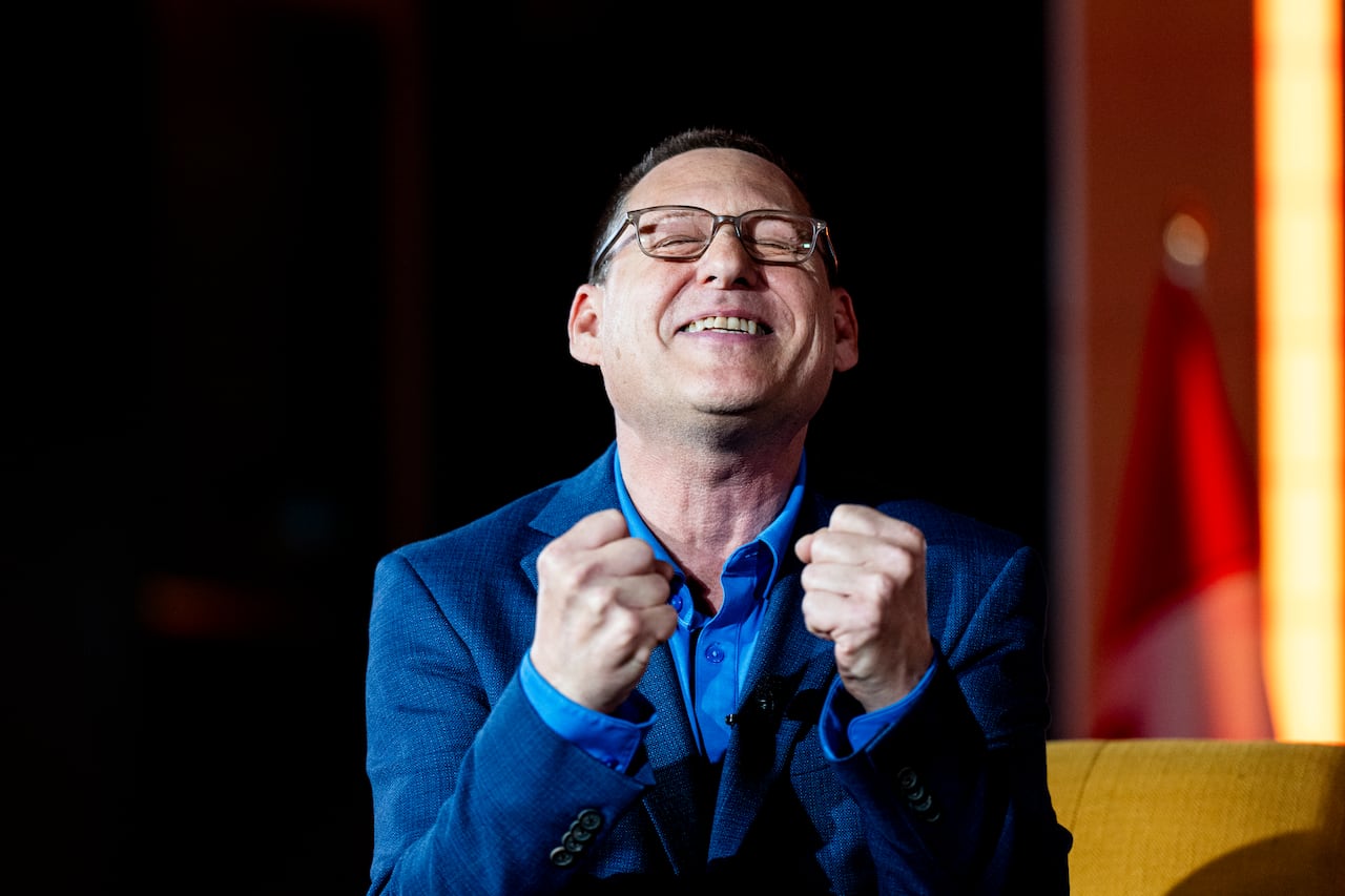 A man in a sports jacket closes his eyes while raising his fists