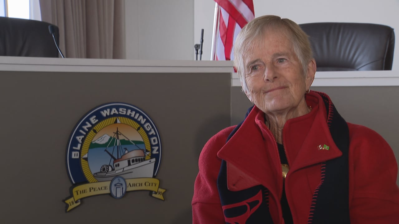 A white woman with short white hair is seen in front of a seal for the City of Blaine, Washington.