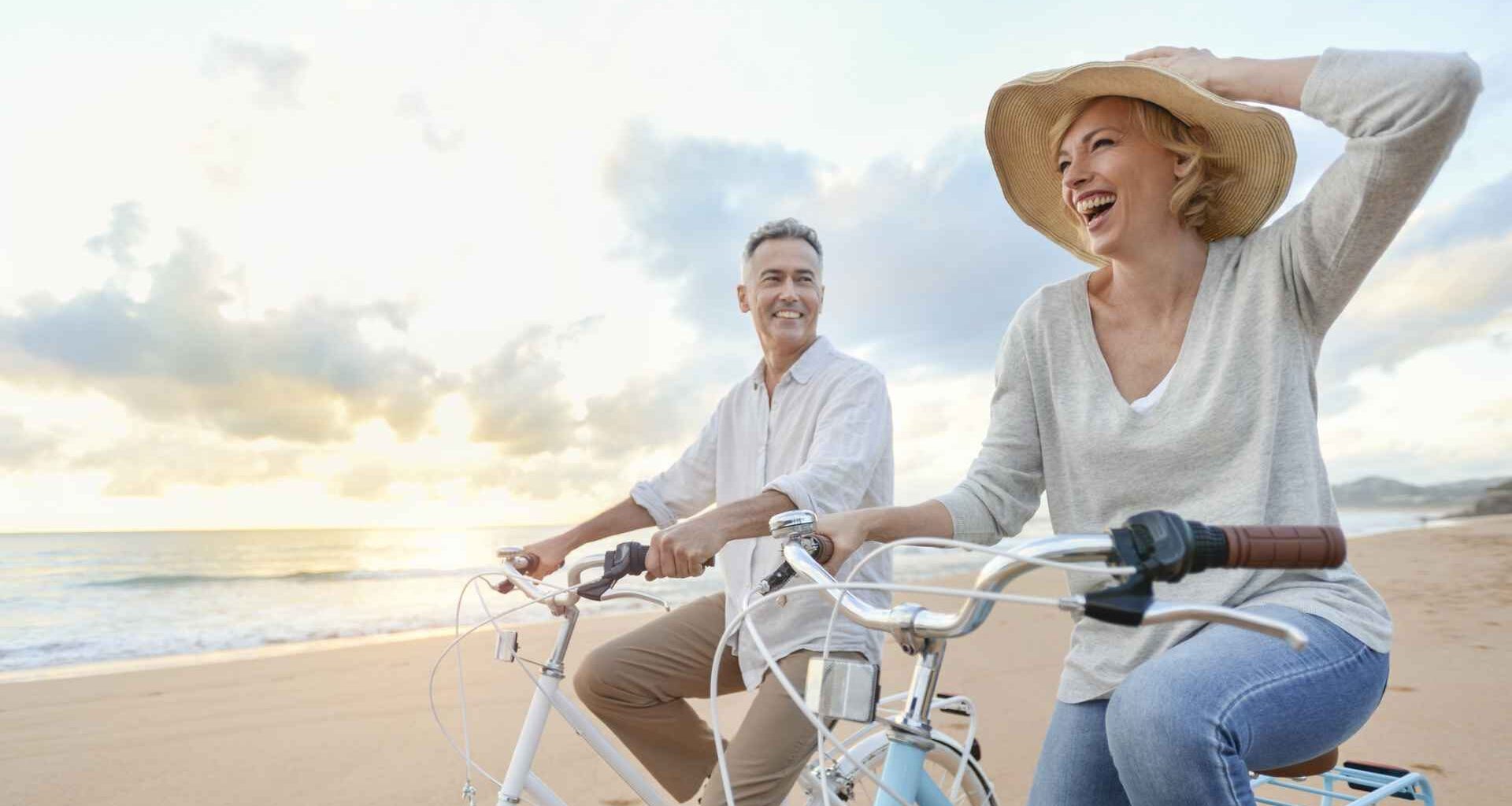 Mature couple cycling on the beach at sunset or sunrise.