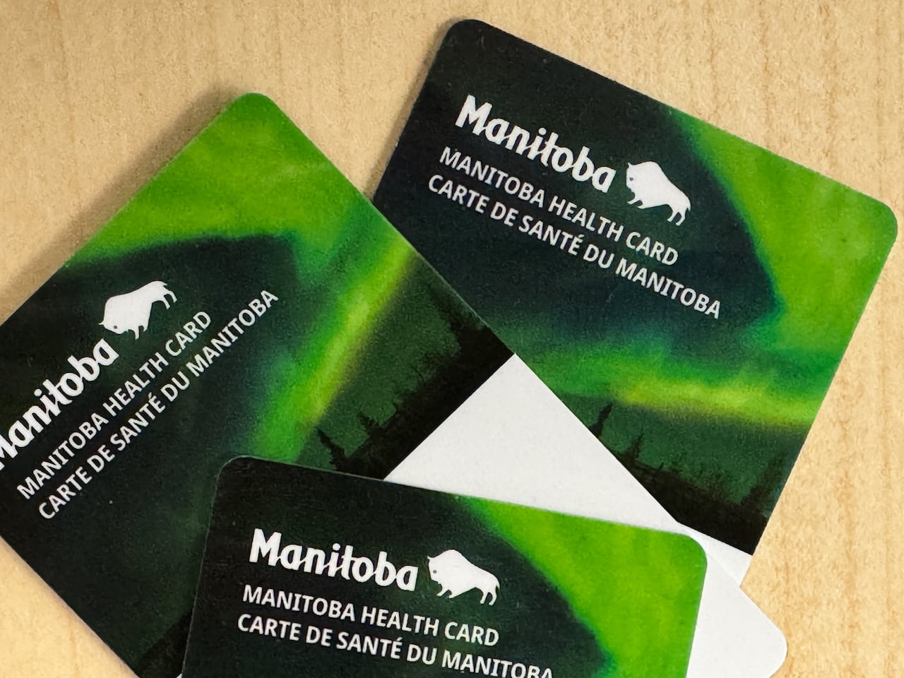 Three plastic Manitoba health cards are laid out on a table.