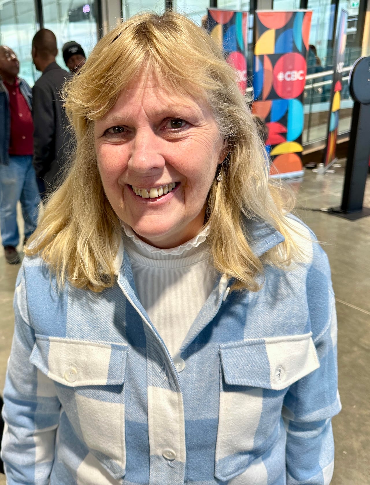 A woman with blond hair smiles as she poses for a camera as a CBC logo is seen in the background.